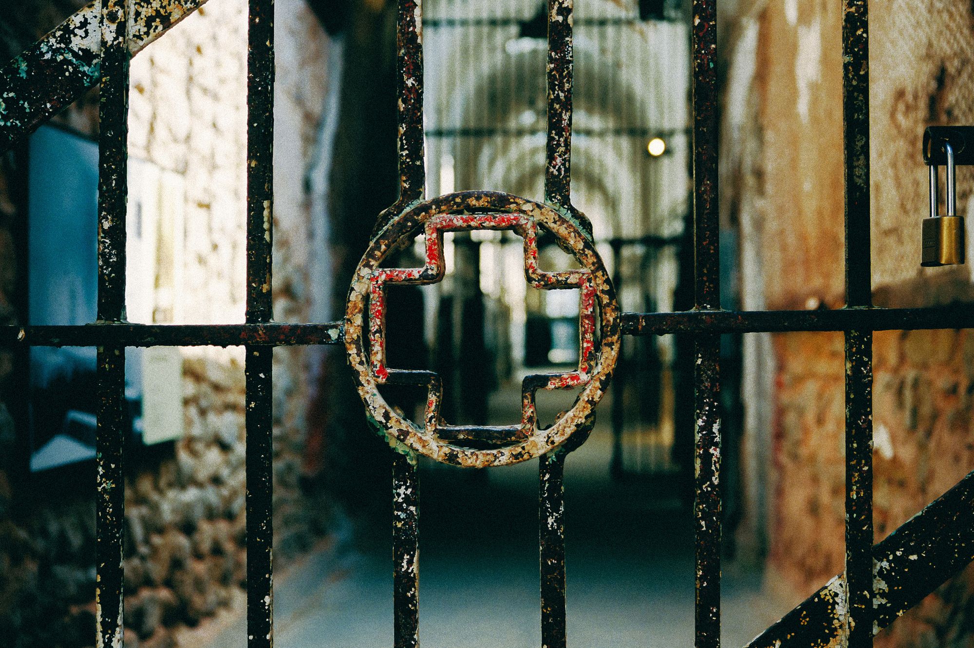 A metal gate has a circle with a red cross symbol at the center. An exhibit can be seen on the wall to the left behind it. 