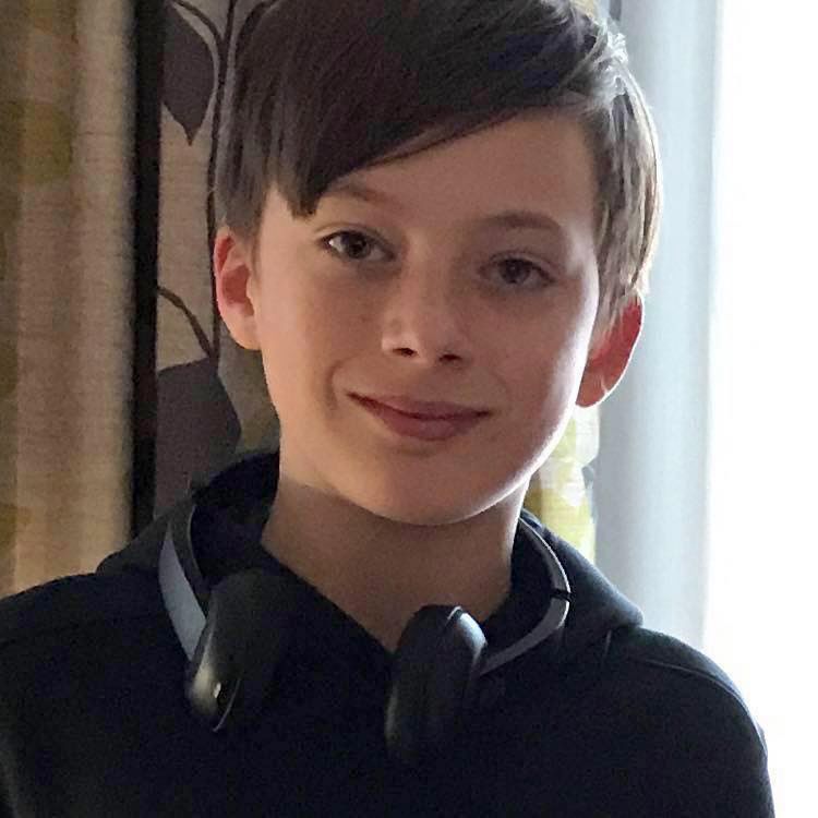 A photo of a teen boy with short brown hair and a dark shirt, and with a pair of headphones around his neck. 