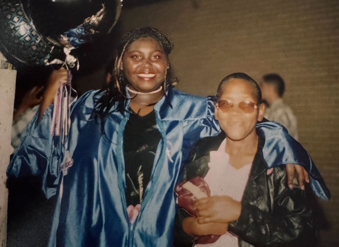 A photo shows Jennifer Wade, a Black woman wearing braids and a blue graduation gown, holding balloons and with her arm around her grandmother, Florine Wade, a Black woman wearing a black coat and a white shirt. 