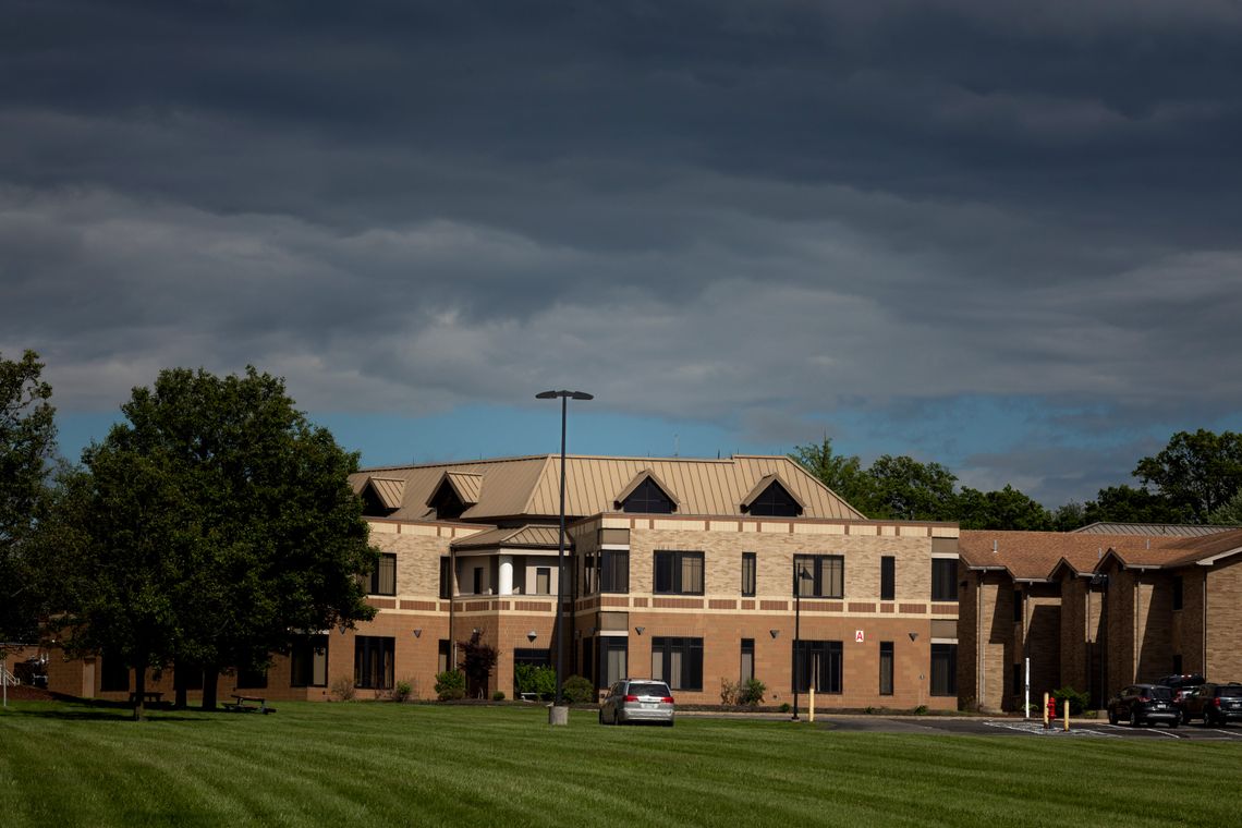 A photo of a multistory tan-and-brown building with a maintained grass lawn.