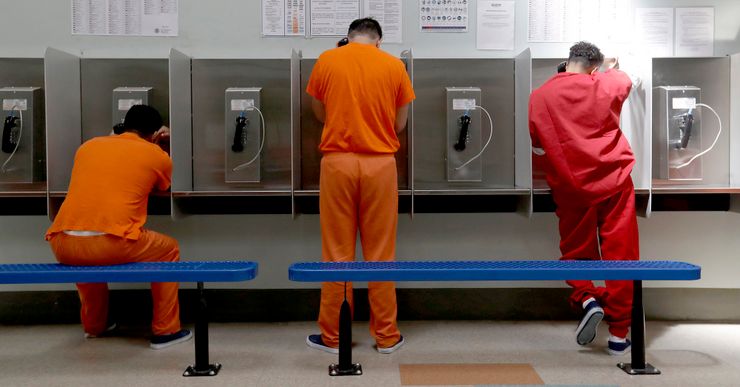 Three men, wearing orange and red uniforms, talk on telephones in a payphone booth area. 