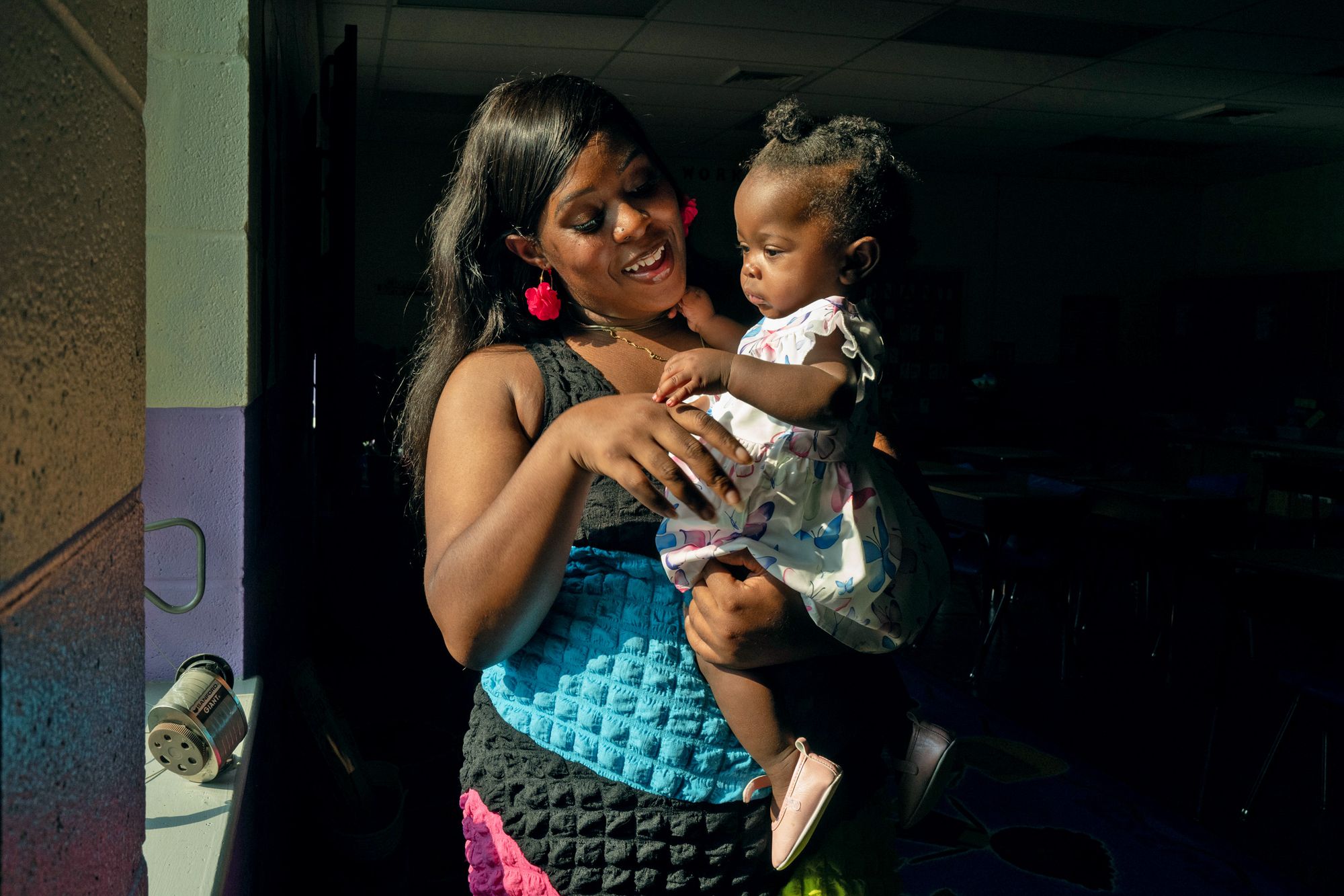 Melissa Robinson, a Black woman wearing a teal blue, magenta and black dress, smiles as she holds her daughter. 