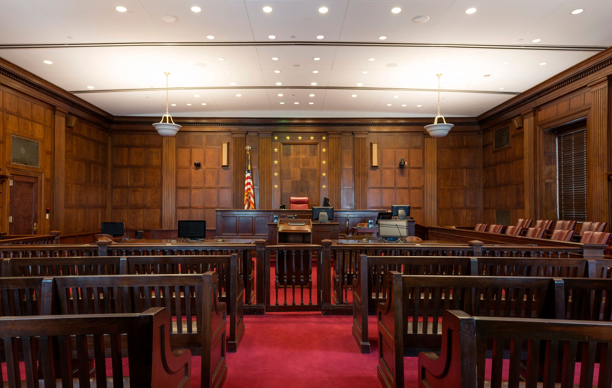 The wood-paneled and red-carpeted inside of an empty courtroom. 