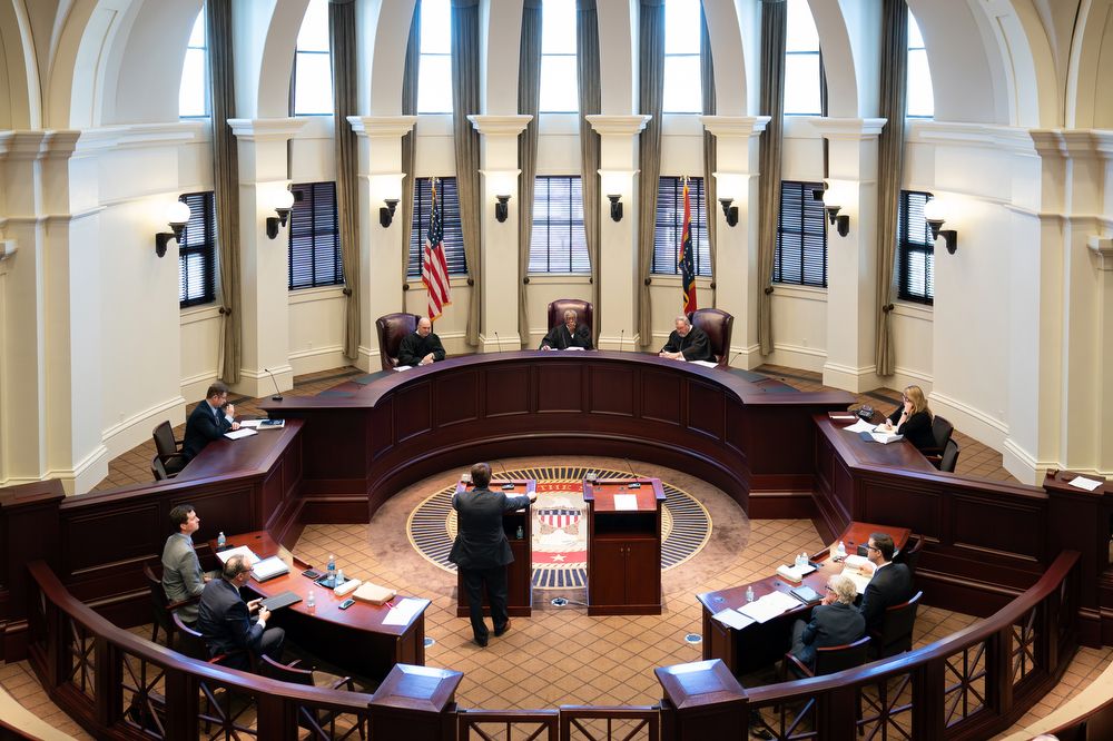 Three judges and various legal council gathered at the Mississippi Supreme Court in a tiled round room with a highly arched ceiling. 