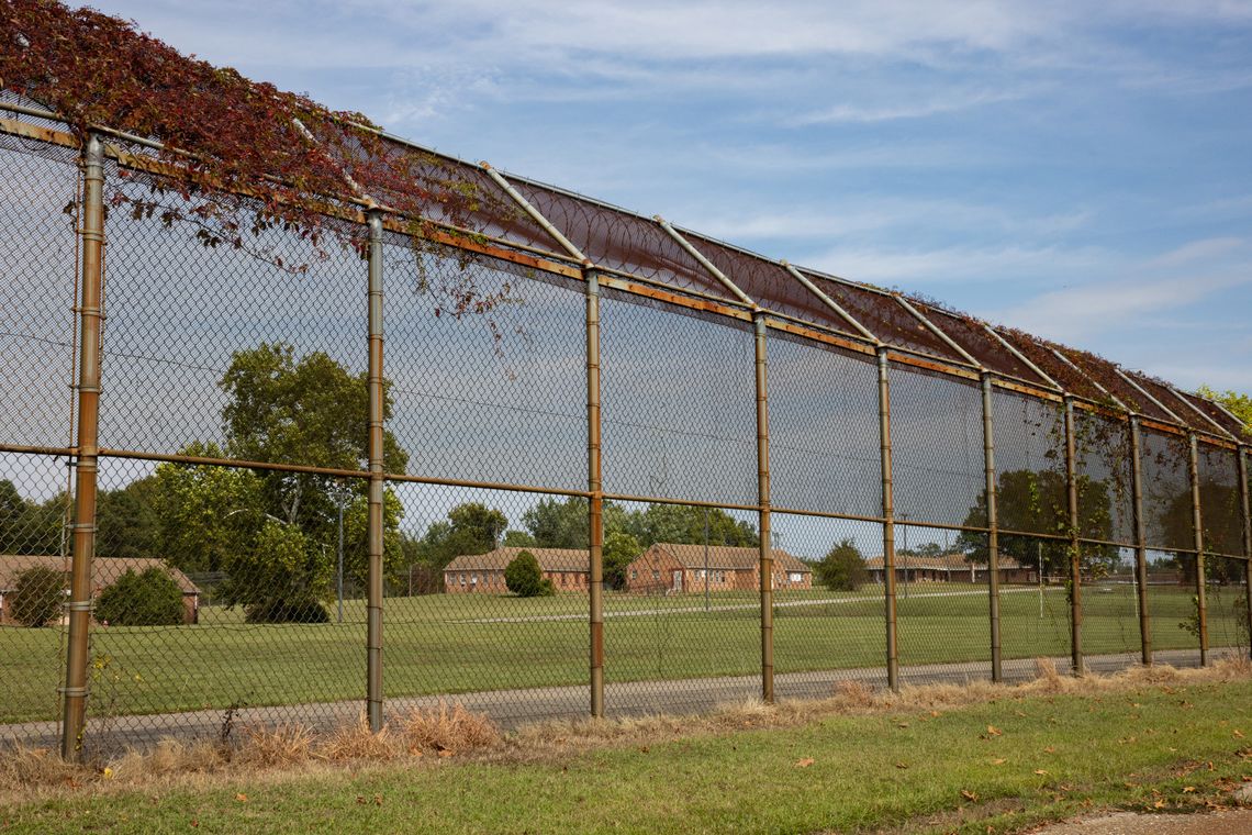 A photo of one-story brick buildings behind a rusted chain link fence.