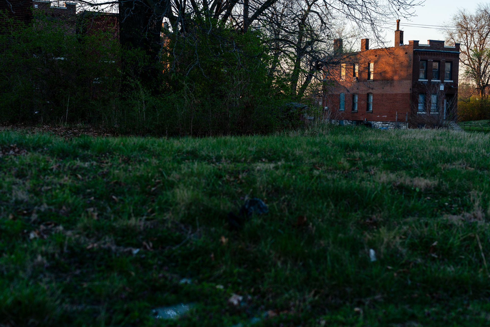 A brick home is pictured in the distance in a green field at sunset.