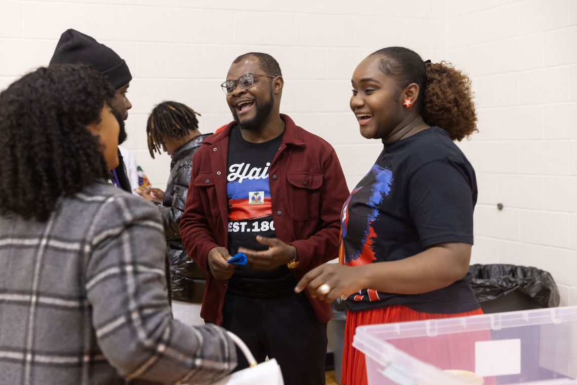 A photo shows a Black man with a goatee and glasses laughing with a group of other Black people. 
