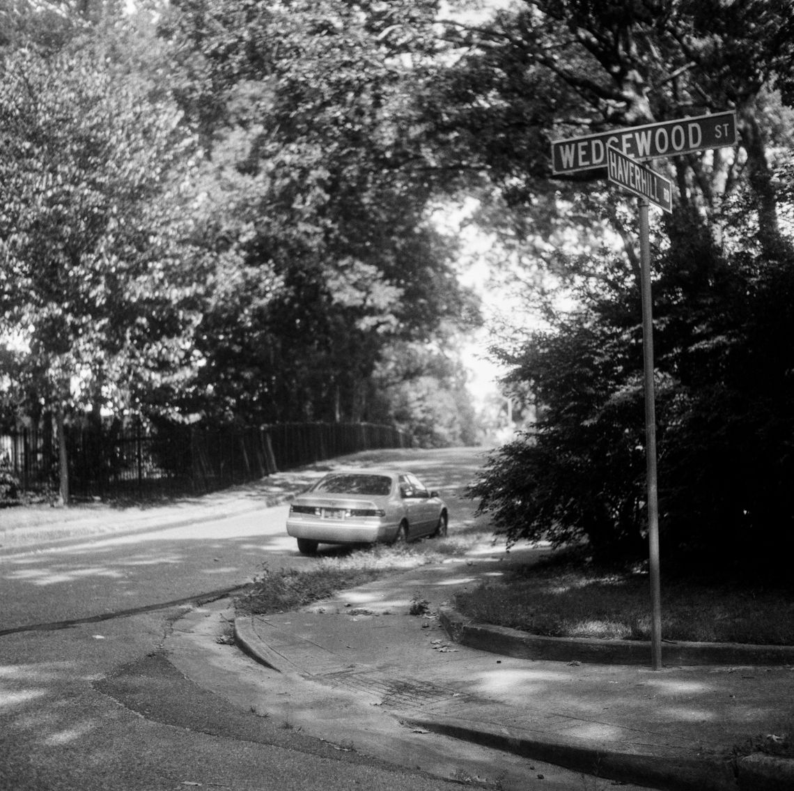 A black-and-white photo of a car parked on a residential road. 