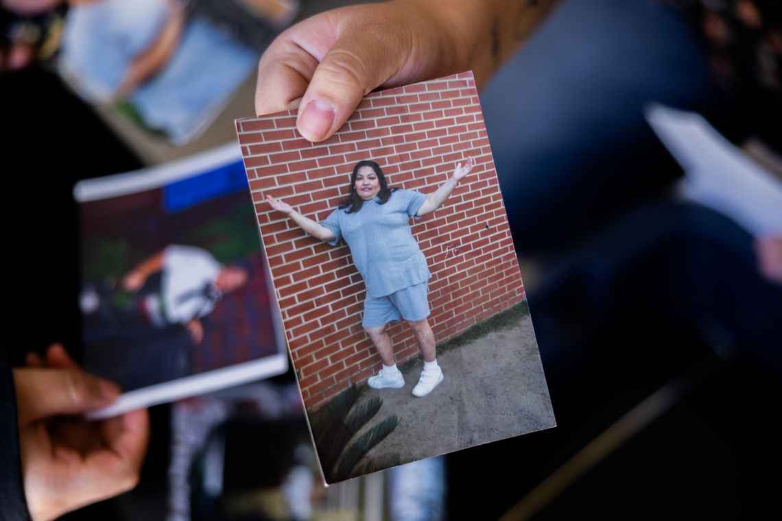 A photo shows a hand holding a printed photo of a woman in a grey T-shirt and grey shorts with white sneakers standing with her arms up.