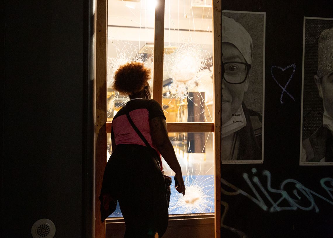 A woman looks through a smashed store window in Soho on Sunday evening. It was one of several retail businesses vandalized or looted. On Monday, major Manhattan stores like Nike and Macy’s were also looted.