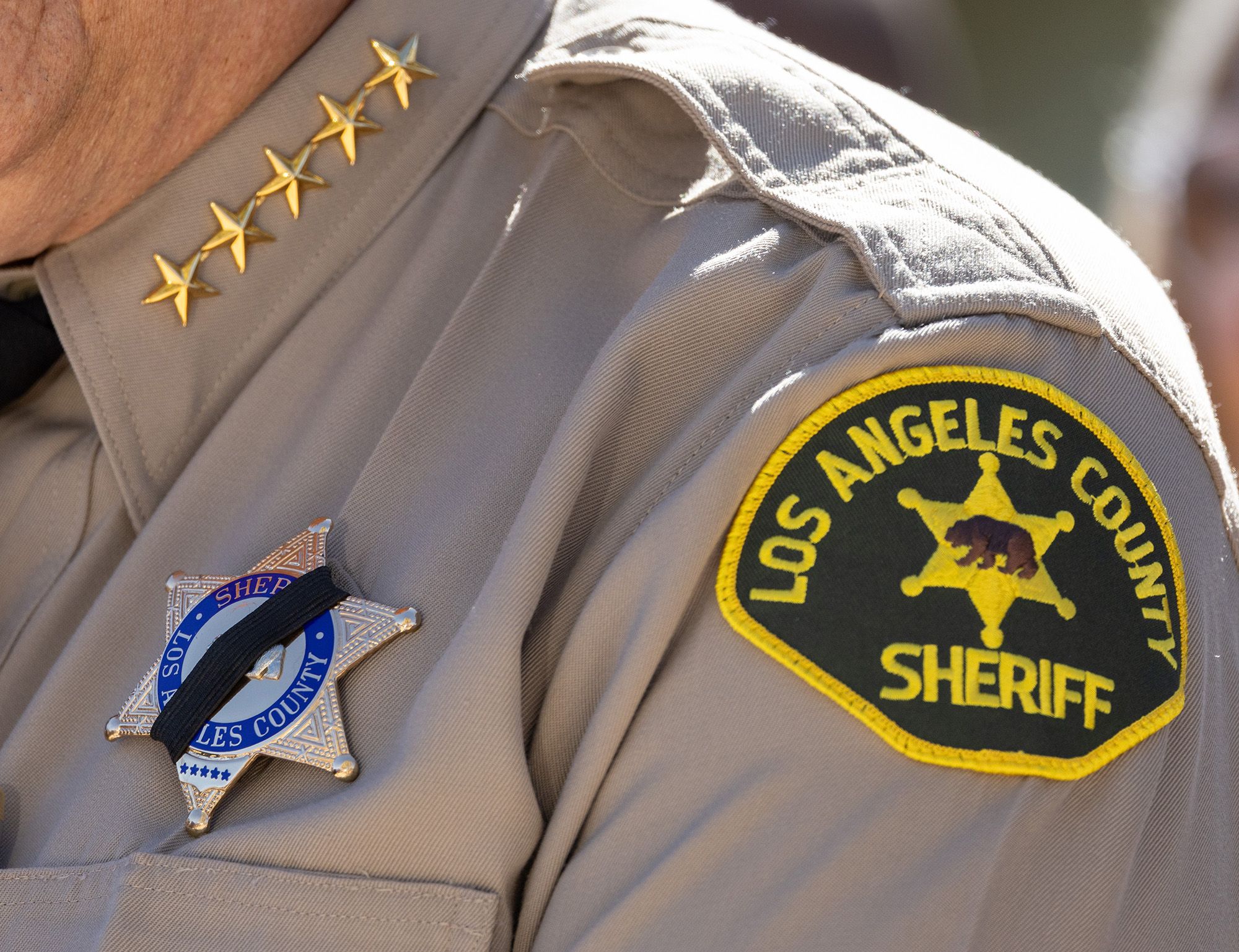 A close-up photo shows a Los Angeles County sheriff wearing a black mourning band over his badge. 