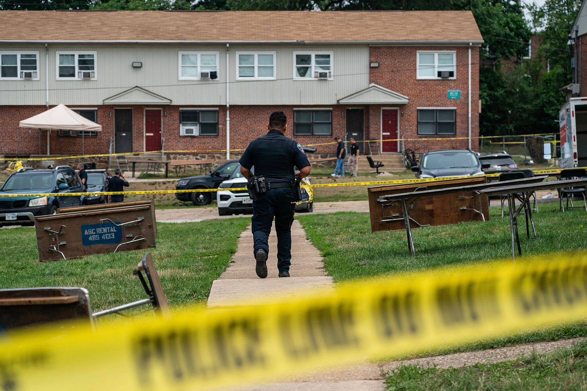 A photo shows a police officer walking through a crime scene investigation surrounded by police tape in a residential area. 