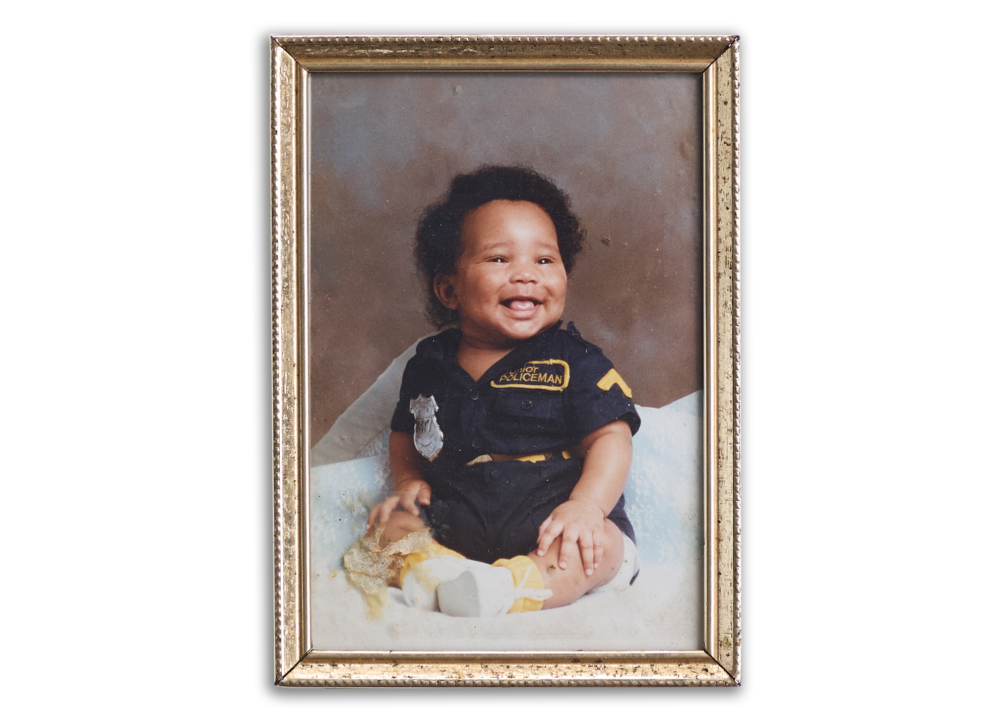 A framed photo of Wilbert L. Cooper, who is Black, as a baby dressed in a tiny police officer’s uniform.