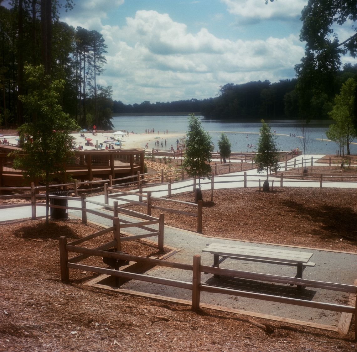 A color photo of a fenced trail with benches at a lakeside park. 