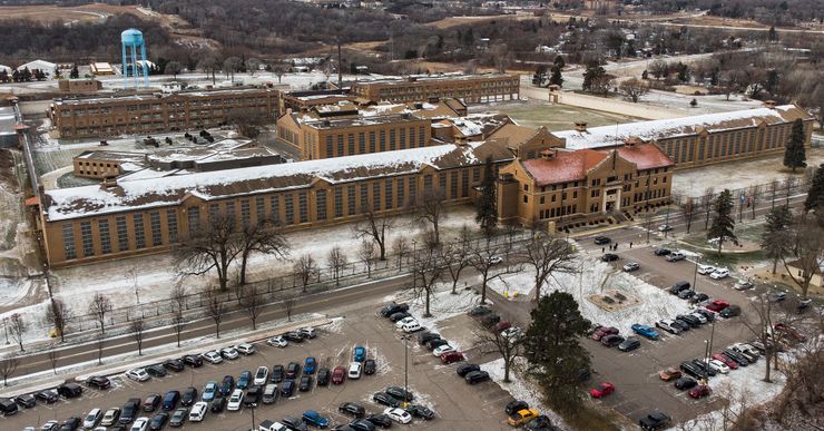 An aerial view of a tan brick prison facility with cars parked in front. 