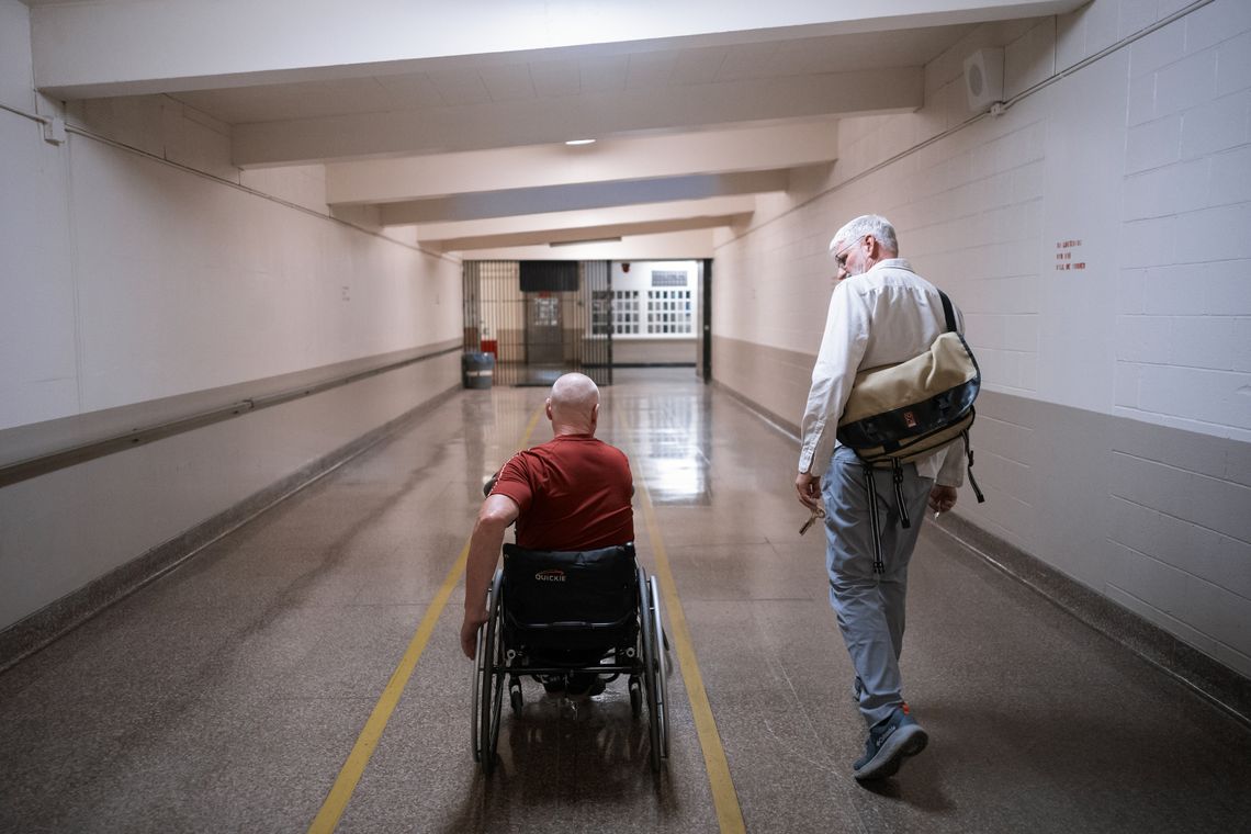A photo shows Coach Jeremiah Holland, a White man, walking down a hall with a person in a wheelchair away from the camera. 