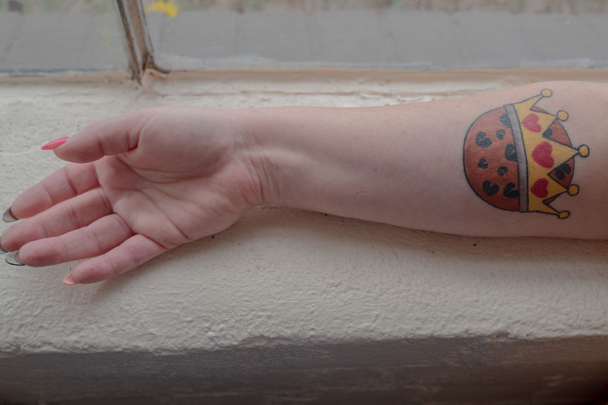 A photo shows Bethney Grove’s forearm on a window sill, showing a tattoo that depicts a cookie with a golden crown emblazoned with three red hearts.