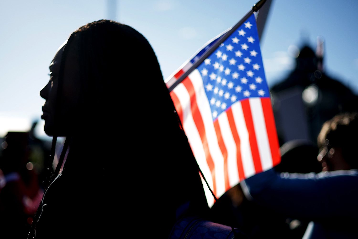 A photo shows the silhouette of a person with long hair, standing in front of a U.S. flag. 