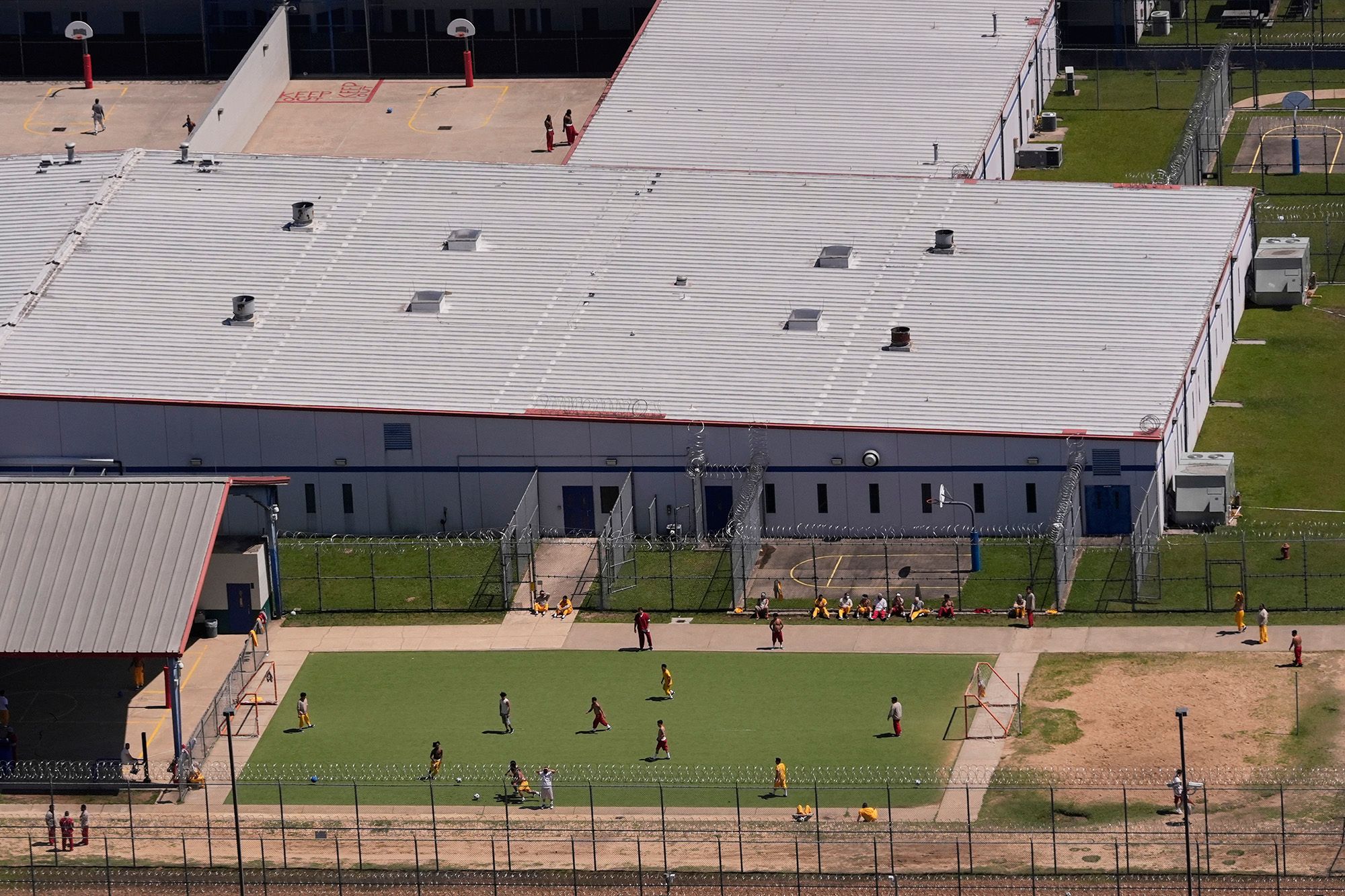 A photo shows an aerial view of people in a field next to a gray building. 