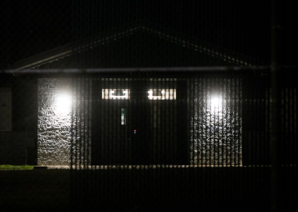 A photo of a building with double doors, seen through a metal gate at night.