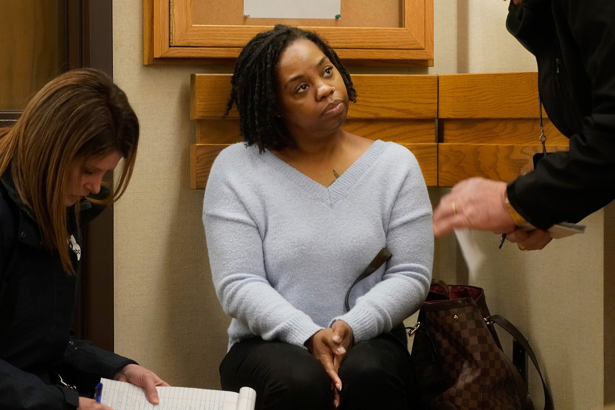 A Black woman with shoulder-length hair and wearing a gray sweater listens to a person not visible in the image, aside from his hands.