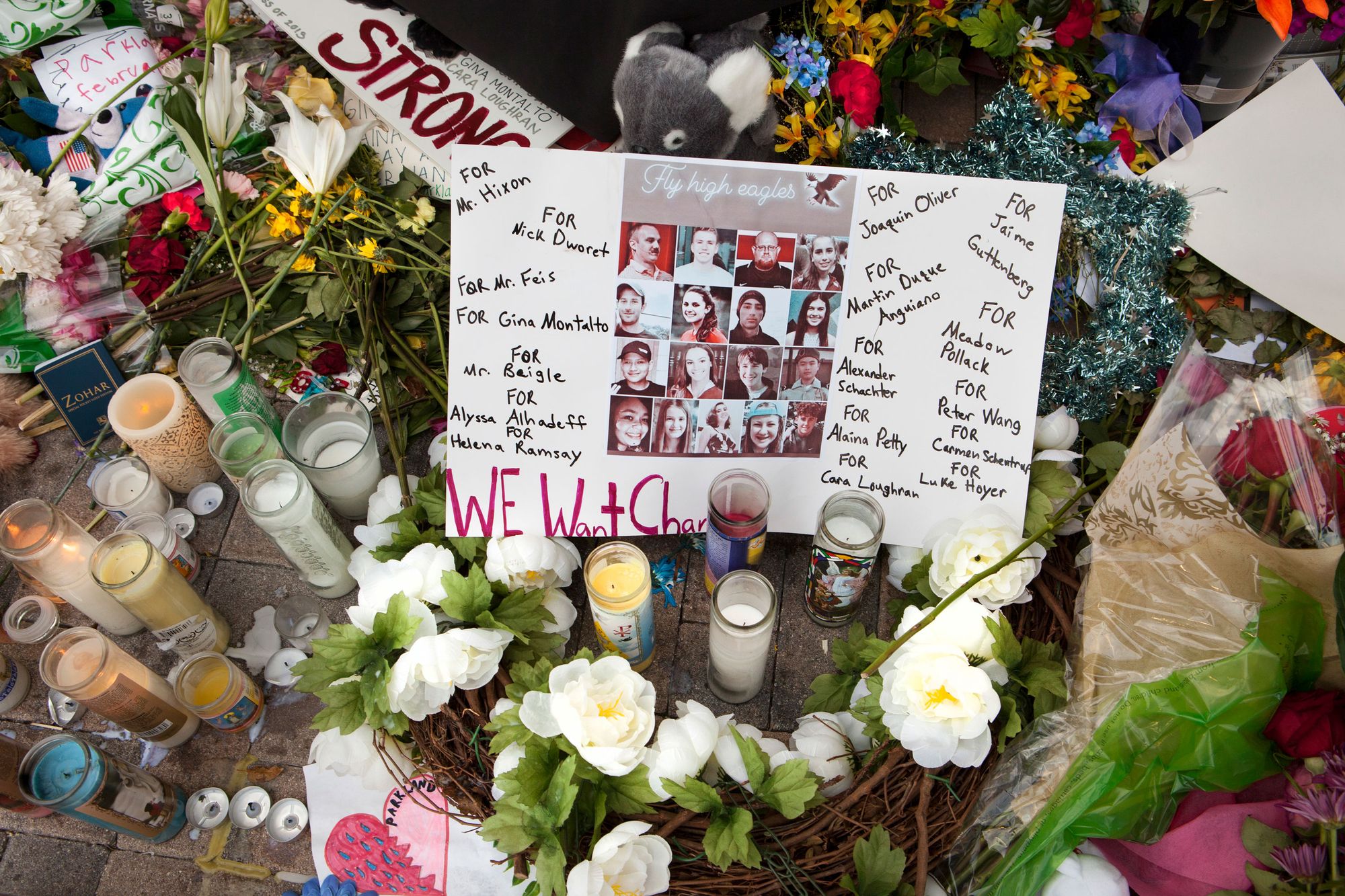 A photo of a poster with portraits of 17 people and their names, surrounded by candles and flowers. 