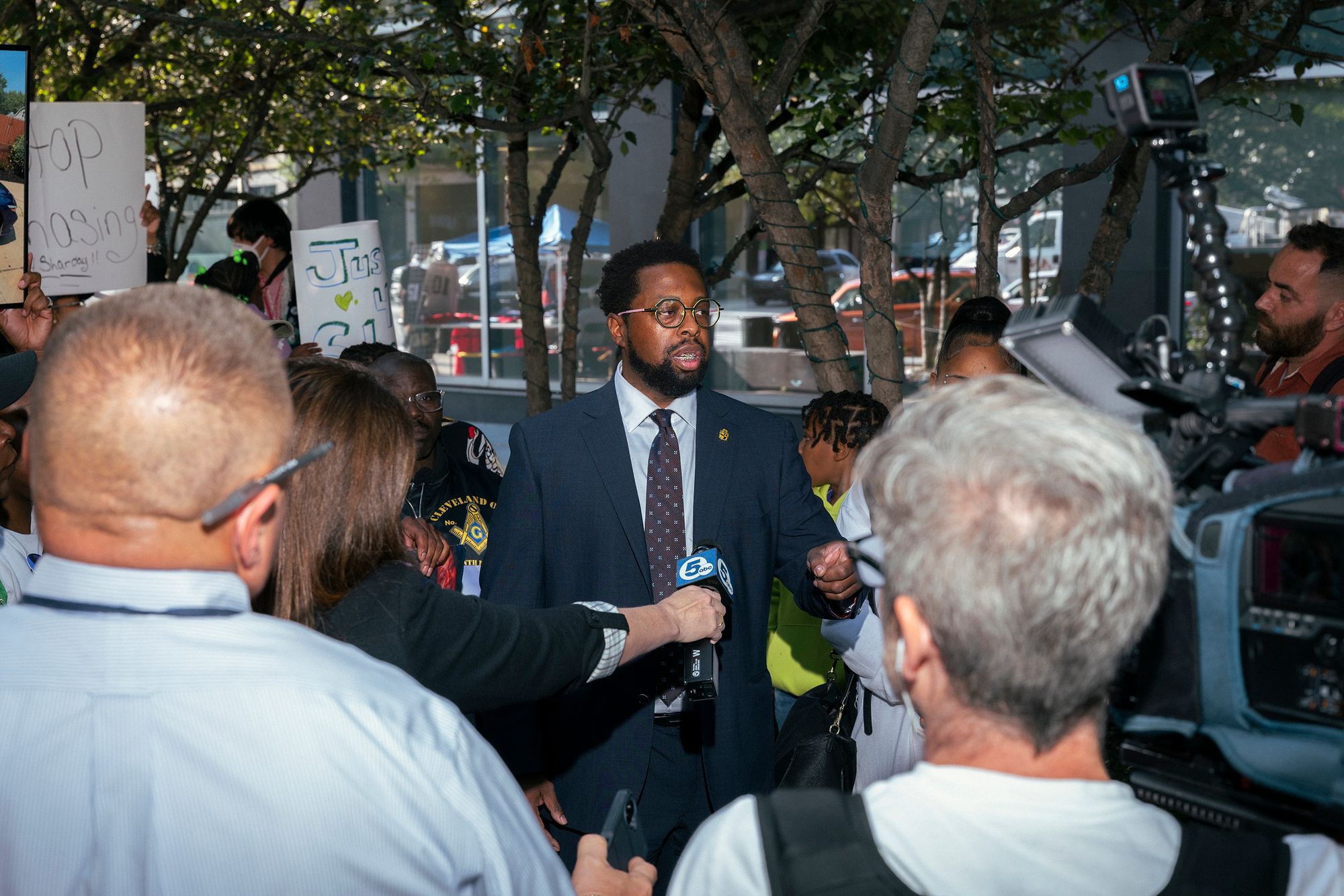 Stanley Jackson, a Black man wearing a suit and glasses, speaks to the press outdoors.
