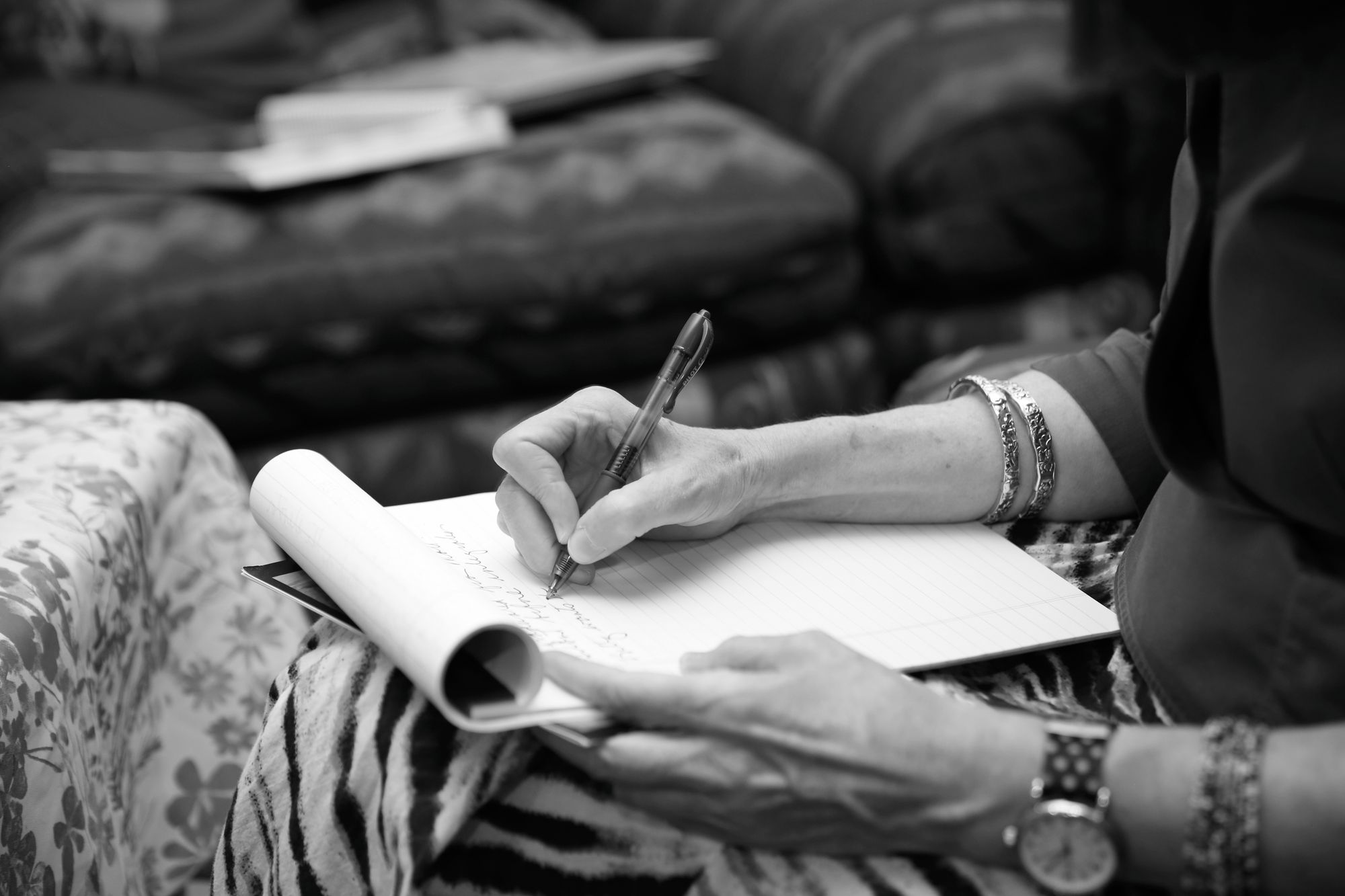 A White woman writes in a notepad on her lap.