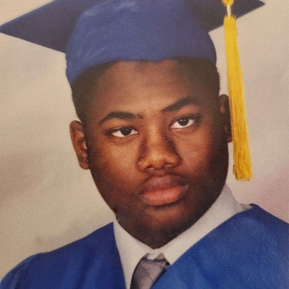 A young Black man in a royal blue graduation robe and cap with yellow tassel. 