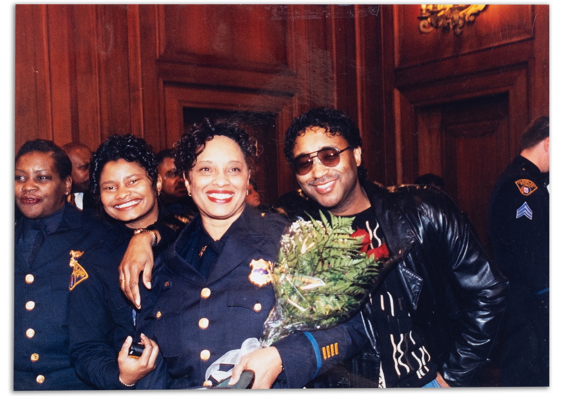 A photo of Satari Smith and Gayle Miller-Cooper, Black women in police uniforms, and Wilbert L. Cooper Sr., a Black man wearing a leather jacket. 