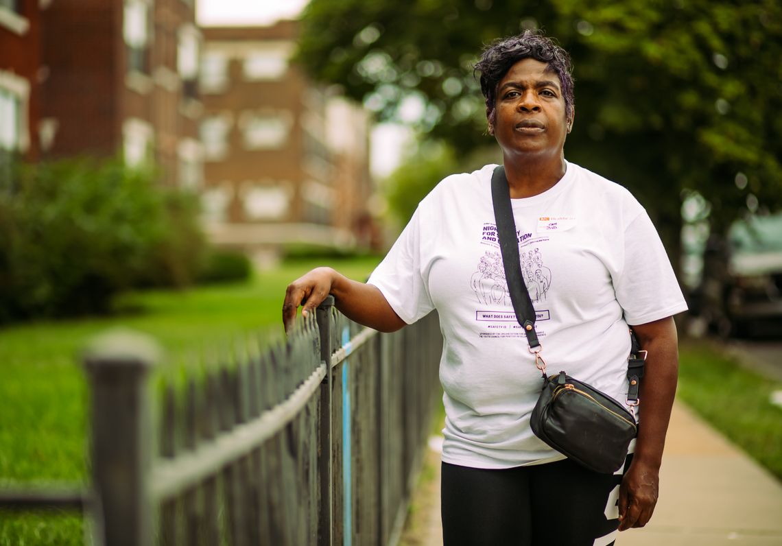 A Black woman with a white shirt and purple hair looks at the camera while holding onto an iron fence.