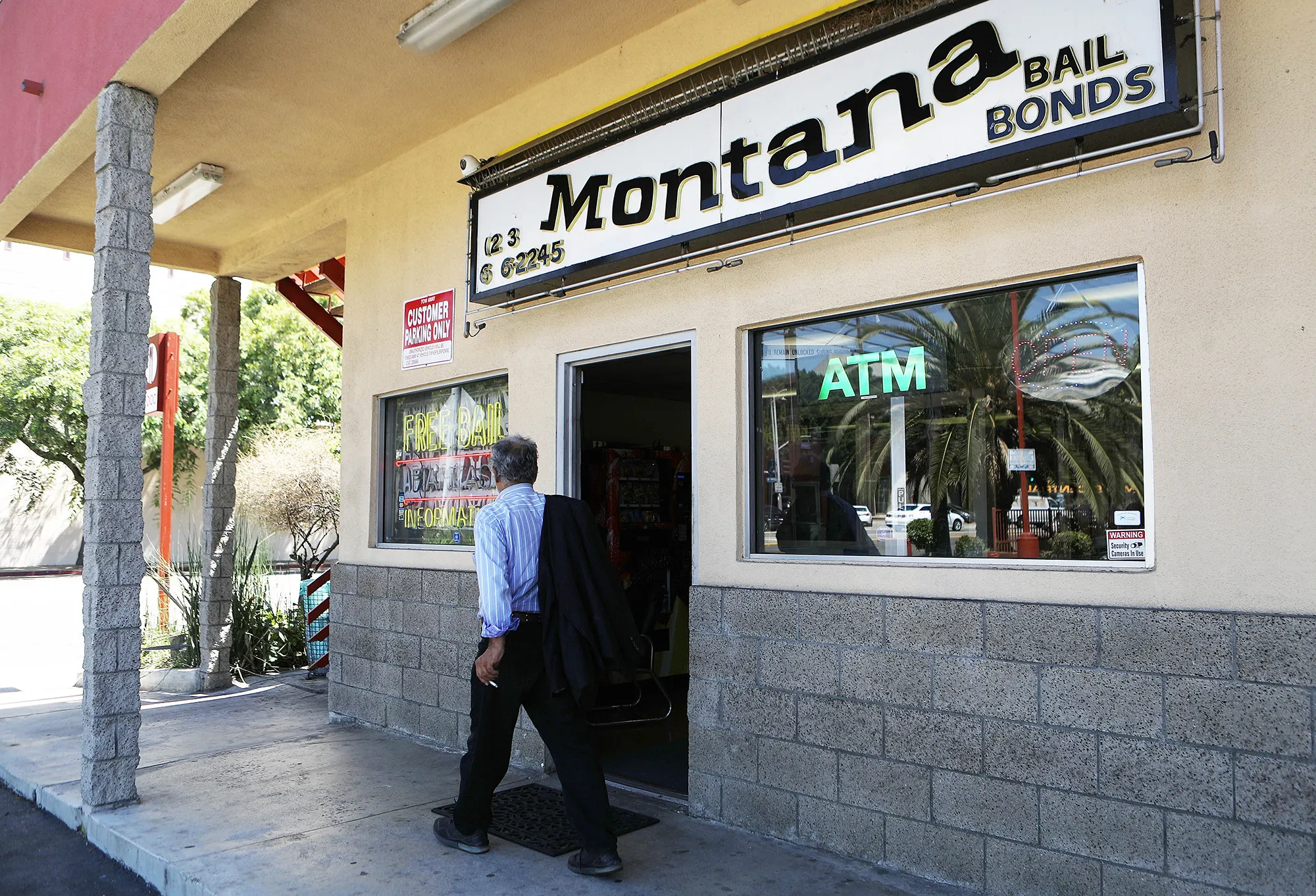 A person, wearing a blue-and-white striped shirt and black pants, walks past a building with a sign that reads "Montana Bail Bonds." 