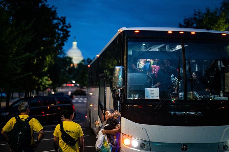 A group of migrants exit from a bus parked in the middle of a street. The U.S. Capitol can be seen in the background.