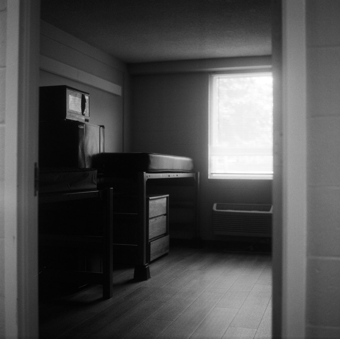 A black-and-white photo of a mattress without sheets in a college dorm room. 