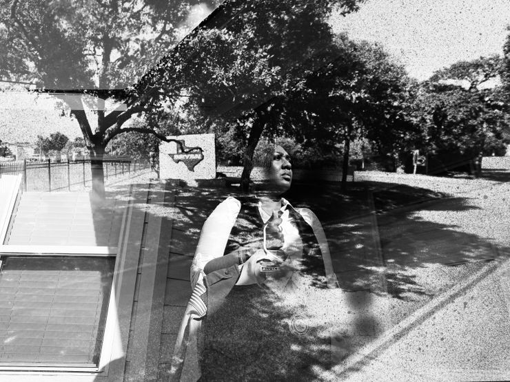 A black and white photo composite shows a photo of a Black woman wearing a white long-sleeved shirt and a black vest holding a uniform, standing in front of a building. In what looks like a double exposure effect, a photo of trees and fencing is visible, as well as an image of the outline of a map of Texas, with the word “Bryan” in the center. 
