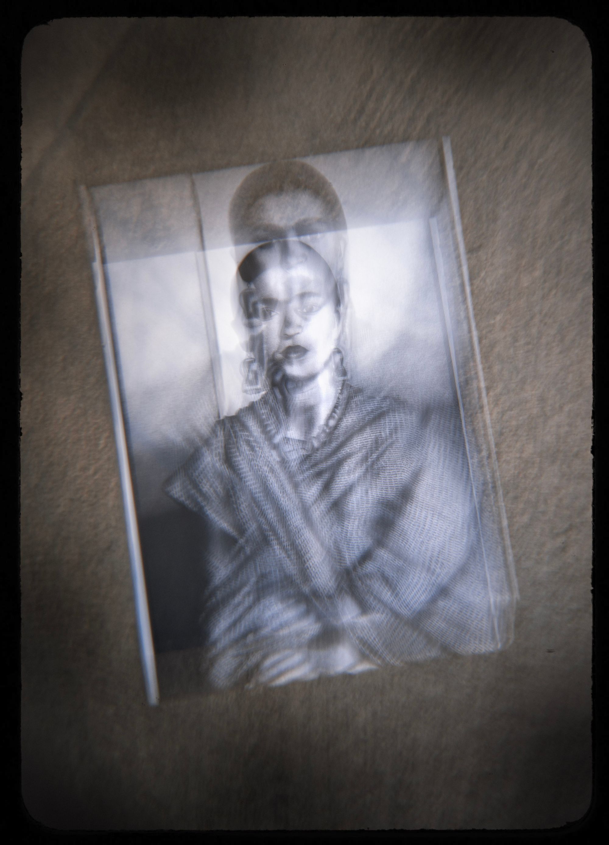 A photo shows a drawing by Frank Reyna of Frida Kahlo, lying on the concrete ground. The photo has a double-vision effect achieved with a special lens. 