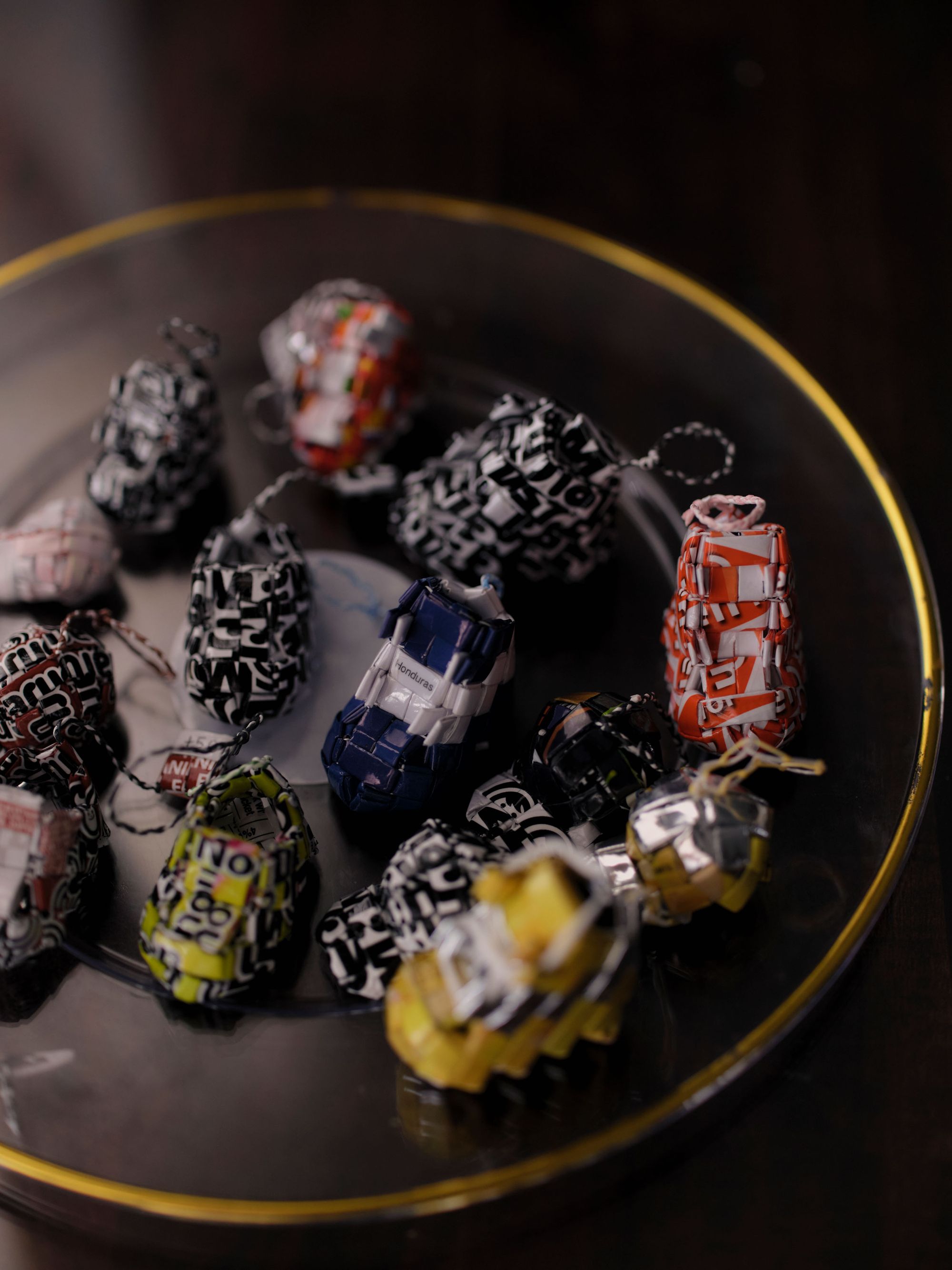 A photo of 12 multicolor keychains in the shape of sneakers, woven together with plastic wrappers. A sneaker in the center of the image reads “Honduras.”