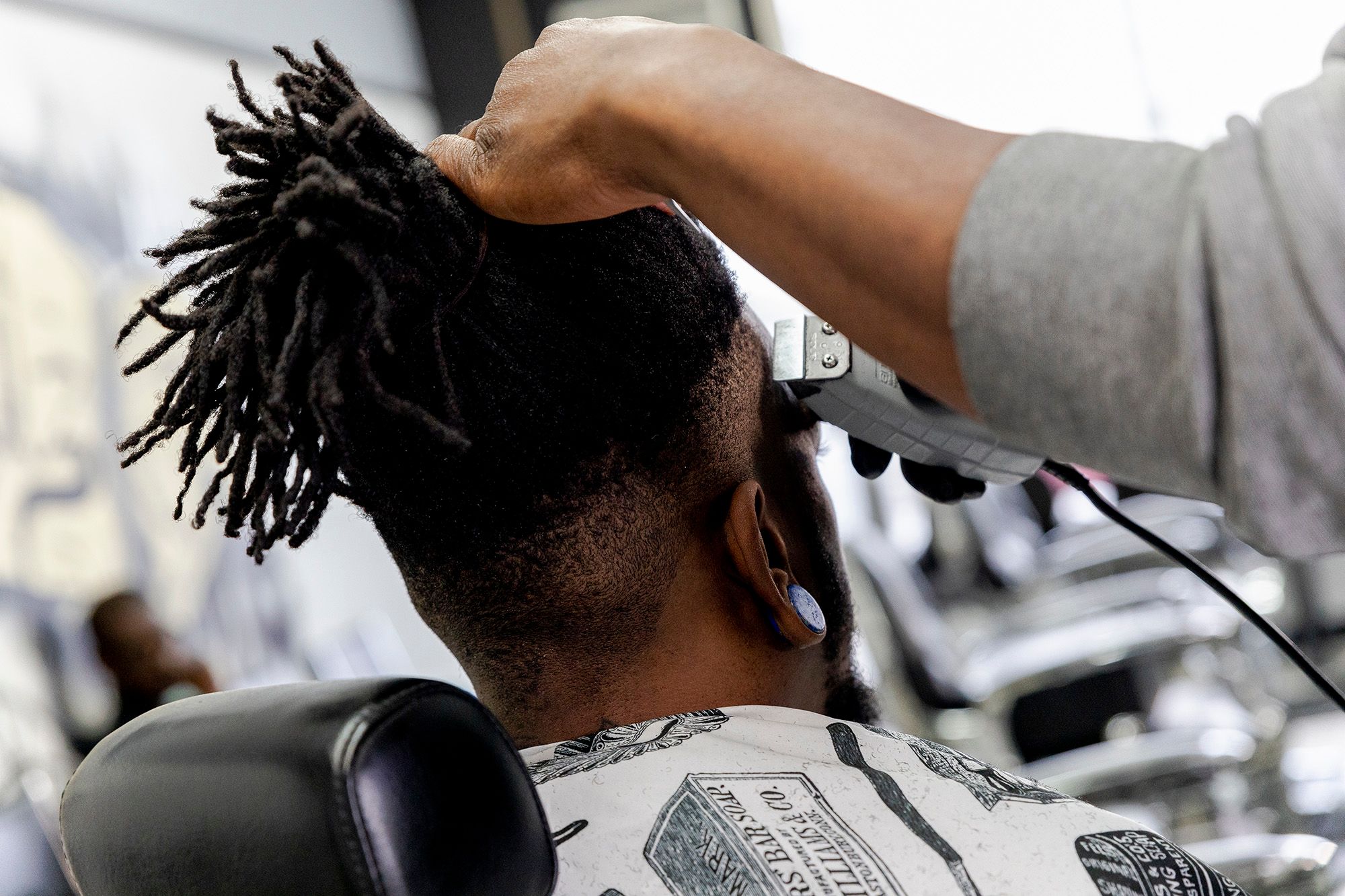 A Black man holds the head of another Black man as he cuts his hair with a clipper. 