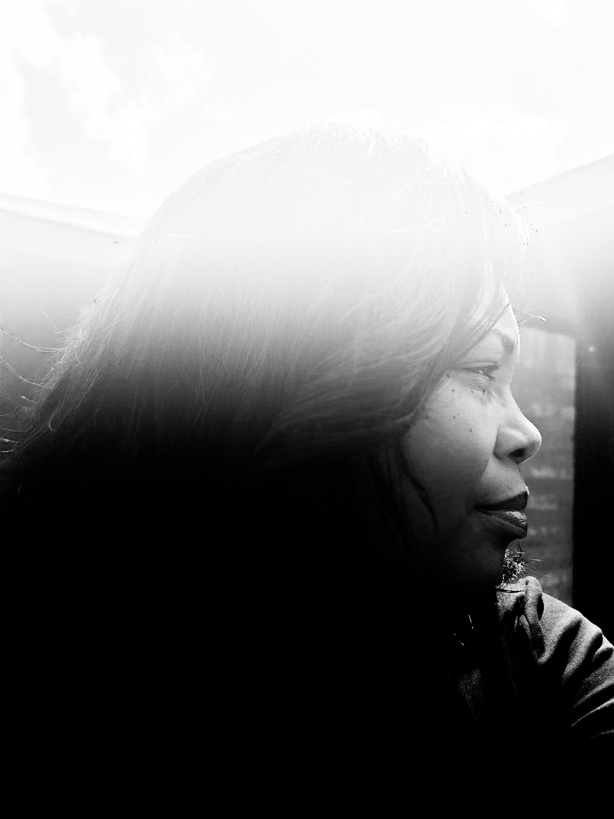 A black-and-white photo composite shows a Black woman in profile looking to the right. There appears to be a light flare at the top of the photo. 