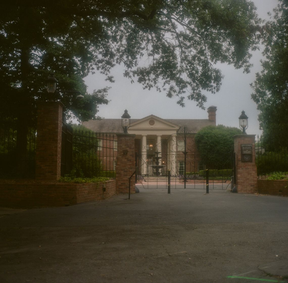 A color photo shows a large brick home beyond a set of gates. 