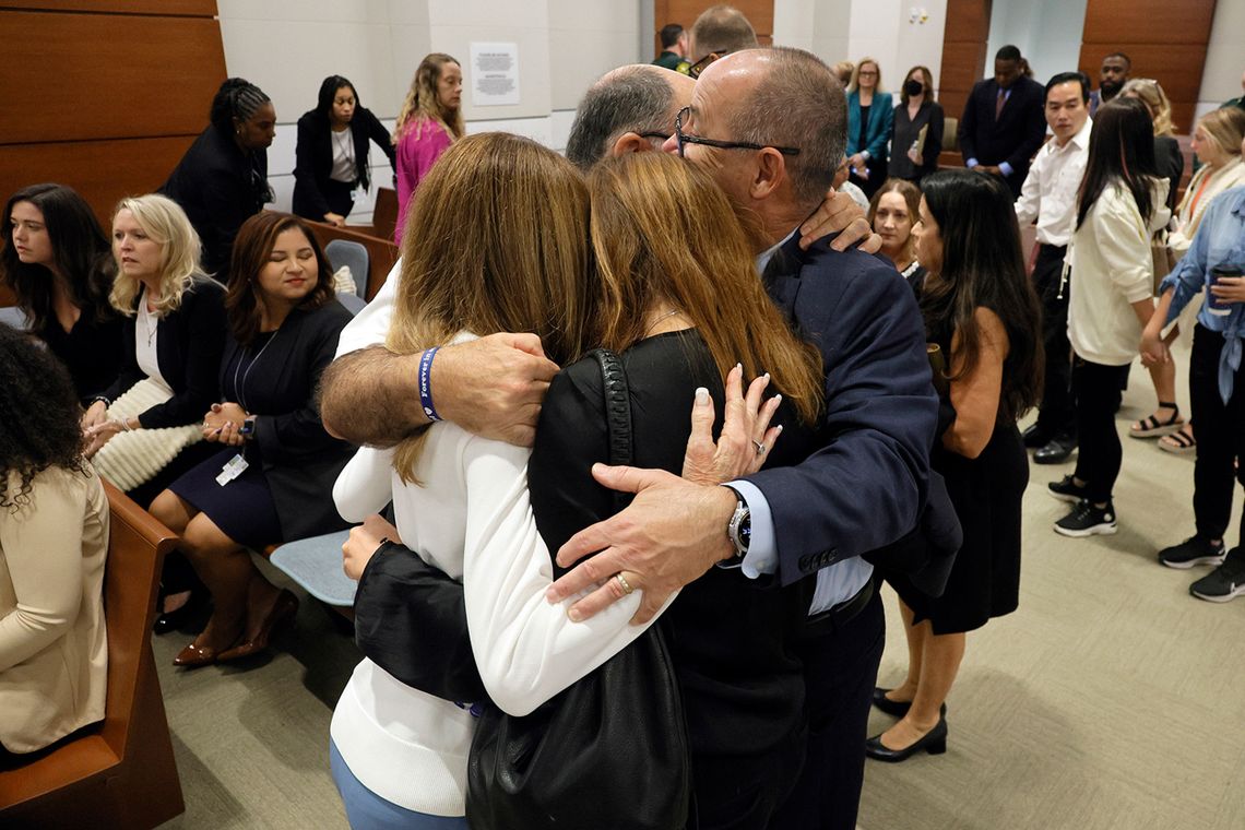 A photo of four people hugging in a courtroom. 