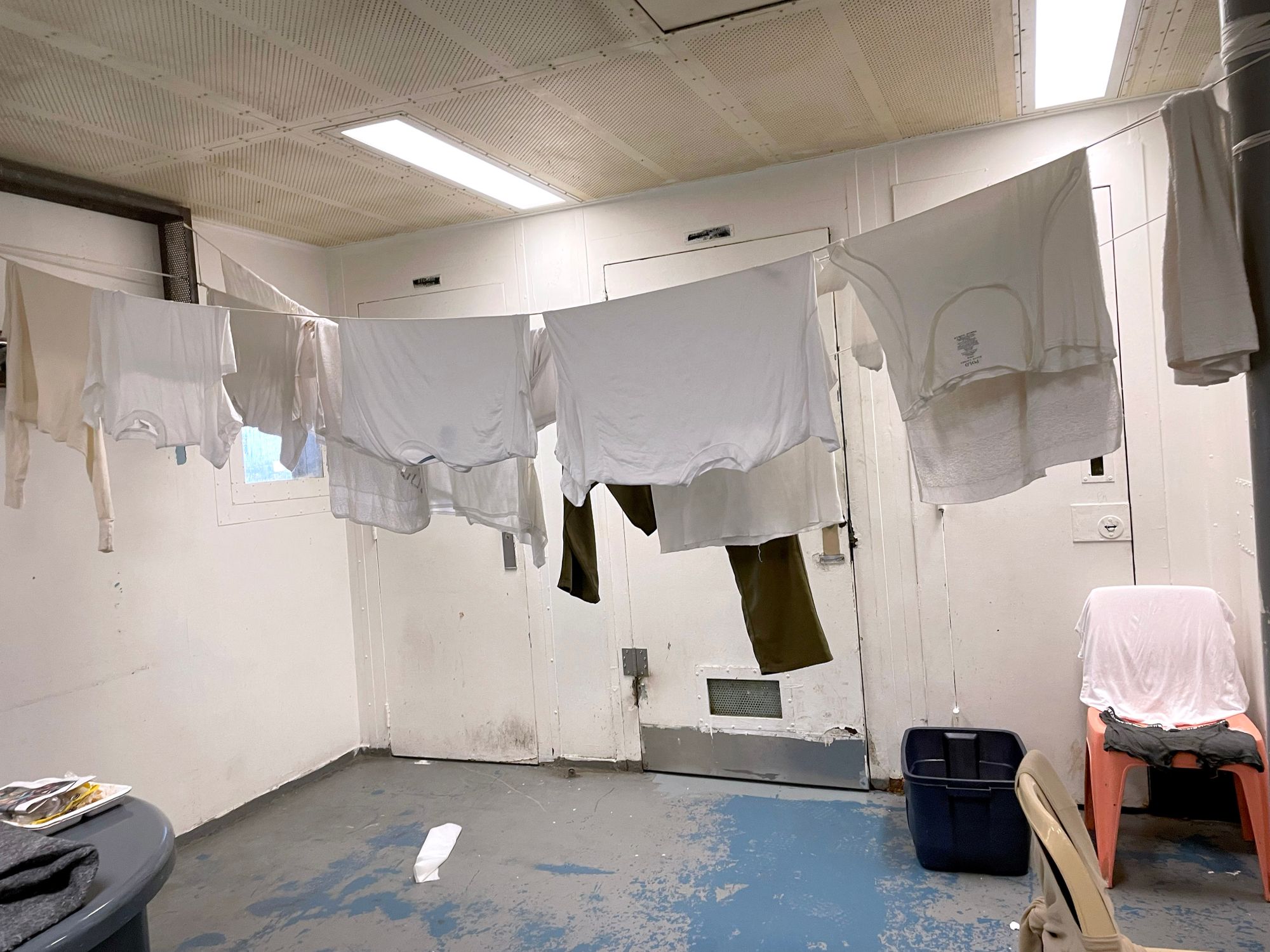 Wet uniforms hang from a clothesline inside a prison room. 