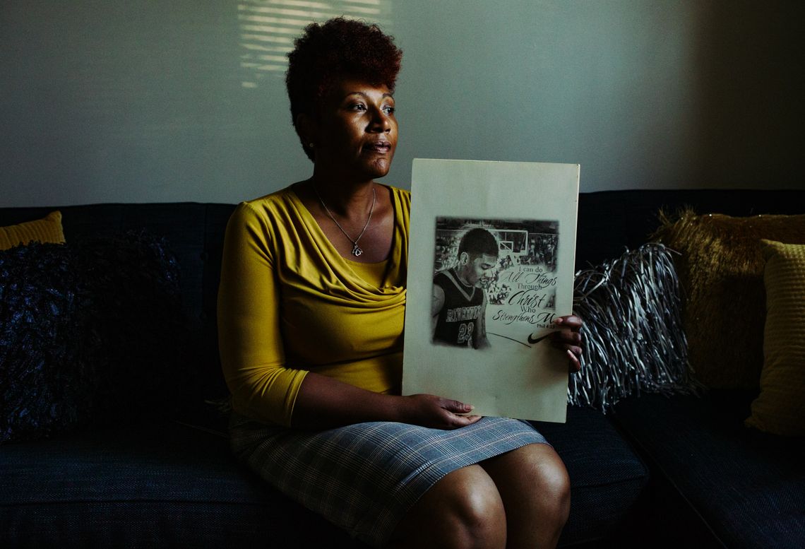 A woman wearing a yellow top and holding a drawing of her son playing basketball.
