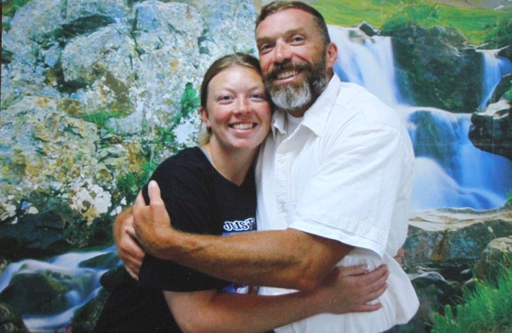 A White woman in a black shirt smiles for a picture as she hugs her father, who is wearing a white prison uniform. 