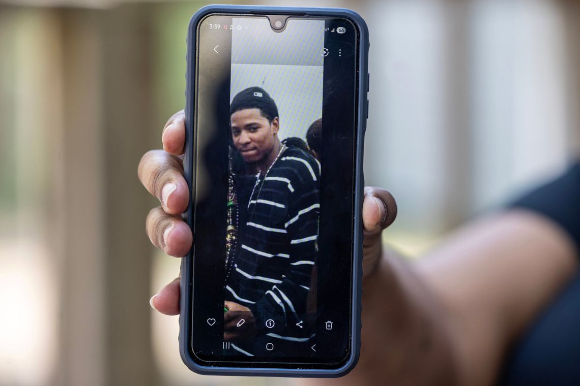 A photo of a Black woman holding up a smartphone displaying the photo of a Black man wearing a striped sweater. 