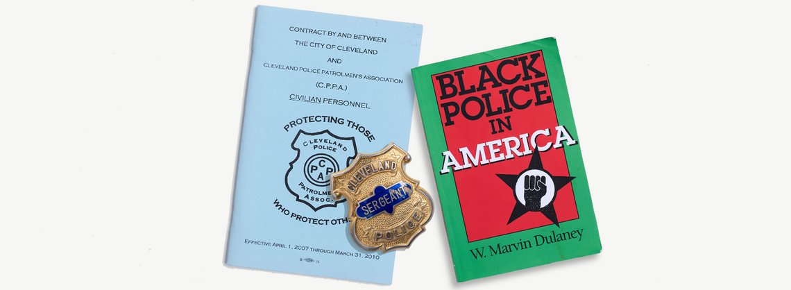 From left, a pale blue booklet with information about the contract between the City of Cleveland and the Cleveland Police Patrolmen’s Association; a Cleveland police sergeant badge; and “Black Police in America,” a book by W. Marvin Dulaney. 