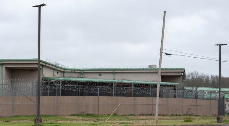 A photo of a beige building with a light green roof behind a barbed wire fence.