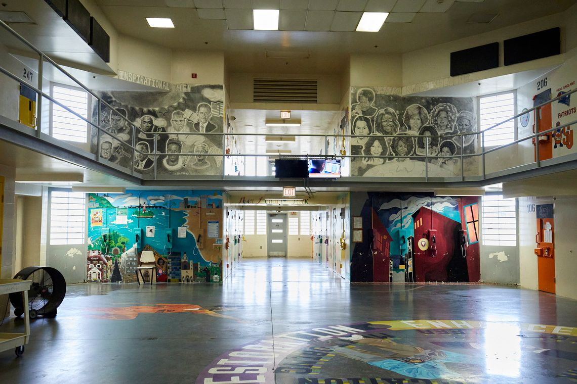 A view of the common area in the interior of the Turbeville Correctional Institution shows a mural labeled “Inspirational Men”, to the left, on the second floor, which shows drawings of Muhammad Ali, Thurgood Marshall, Tupac Shakur, and former President Barack Obama, among others. To the right on the second floor, a mural labeled “Women of Influence” shows Maya Angelou, Rosa Parks, former First Lady Michelle Obama and Sojourner Truth, among others. On the lower floor, on the left side, there is a painted mural of a beach scene in blues and greens and yellows, and on the right side there is a painted mural of a scene with buildings, mostly in shades of reds and blues.