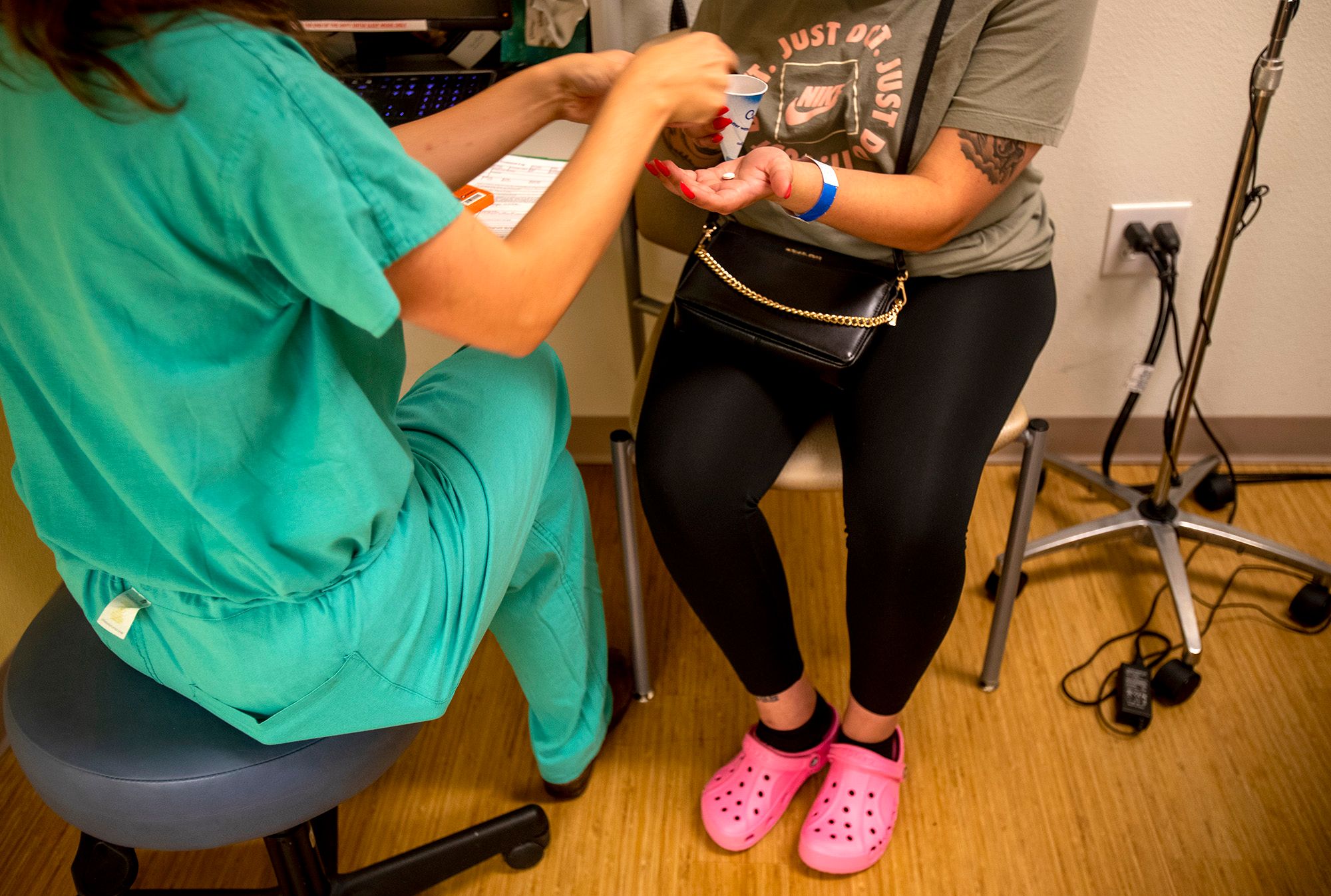 A medical resident, who is sitting on a stool in front of a desk, gives a woman medication to terminate her pregnancy. 