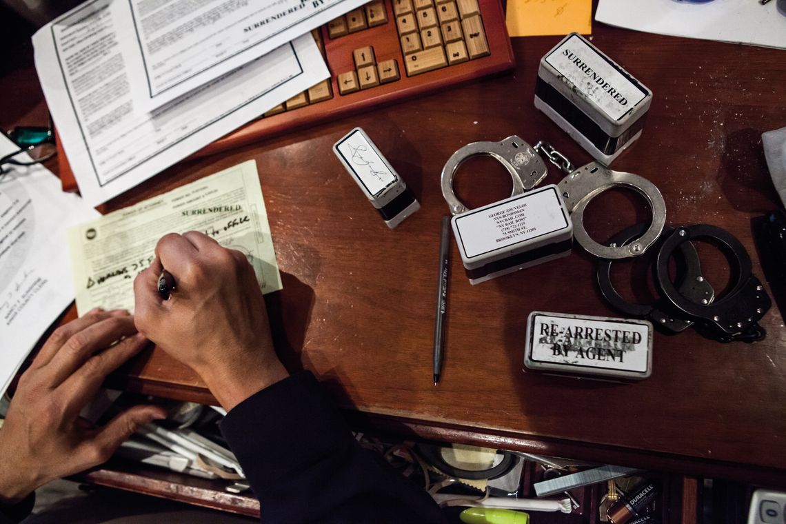 Handcuffs, stamps, and documents cover Zouvelos’s desk.